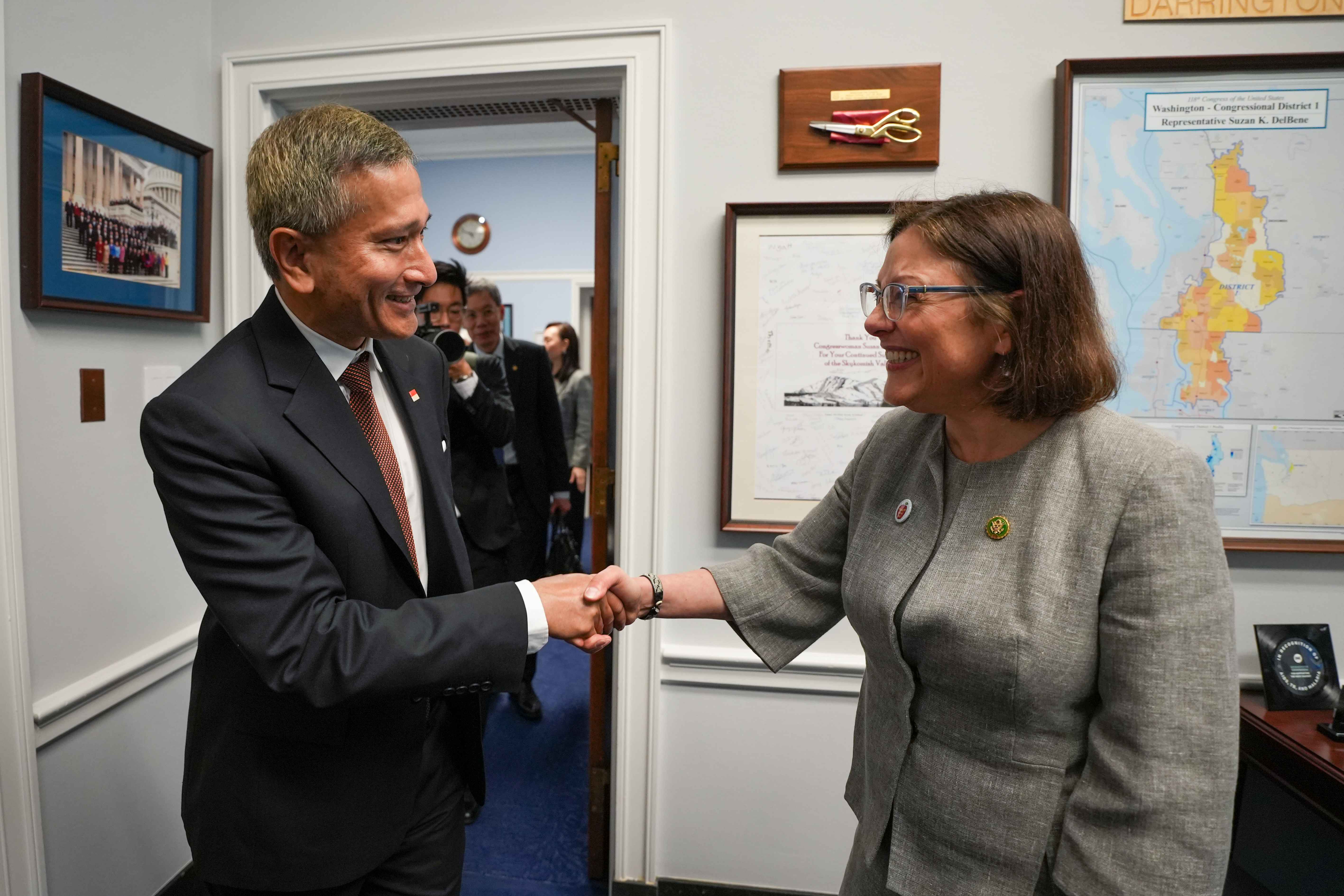 Man and Suzan DelBene shaking hands in an office with framed maps.
